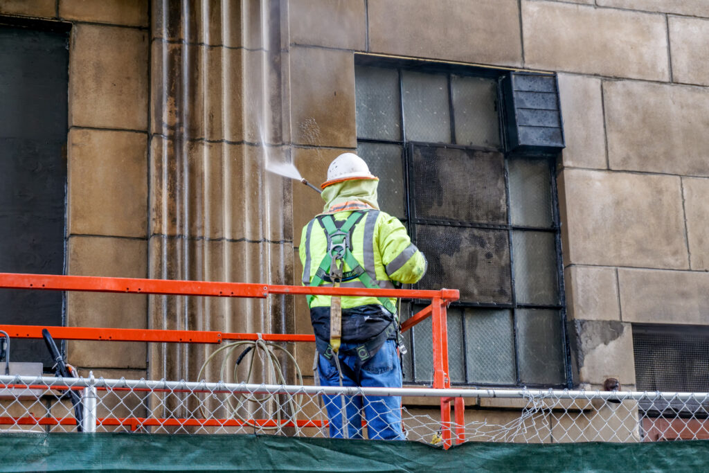 Workman power washing a building's exterior
