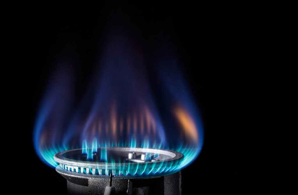 A gas range is lit against a black backdrop. The flame is a mix of blues and oranges.