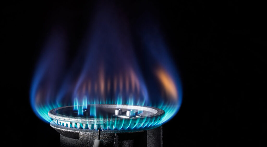 A gas range is lit against a black backdrop. The flame is a mix of blues and oranges.